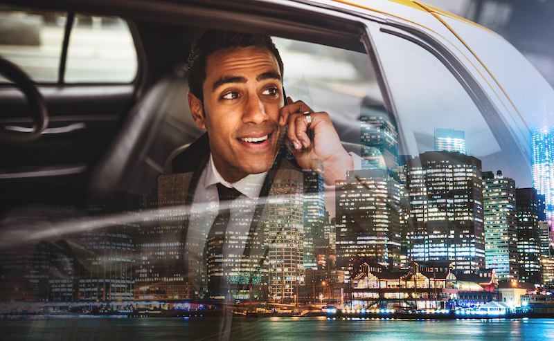 A passenger on a phone call in the back of a taxi at night, city lights behind