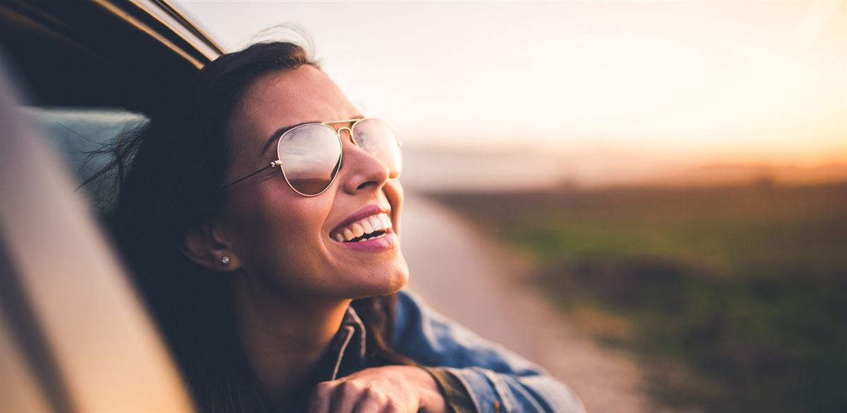 A smiling passenger looking out of a car window at sunset